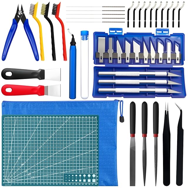 Kit disposto: tronchesino, tre spazzole, aghi, sbavatore e dieci lame, due raschietti, un set di coltelli in un astuccio blu, un tappetino da taglio, una bustina con zip, tre lime e una pinzetta
